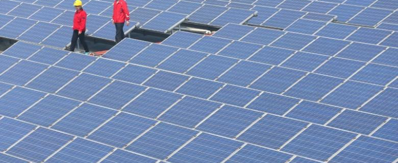 Workers walk past solar panels in Jimo, Shandong Province, China, April 21, 2016. China Daily/via REUTERS